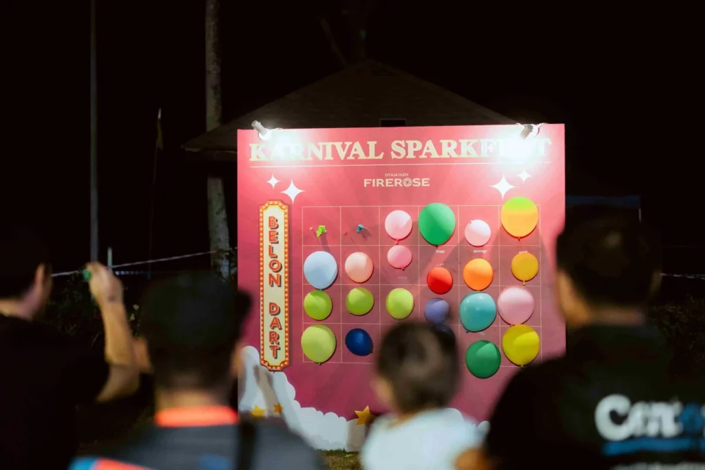 Spark Fest Carnival l Karambunai Hotel 6 Players aim darts at colorful balloons on a carnival game board during a nighttime outdoor gathering in Karambunai Hotel