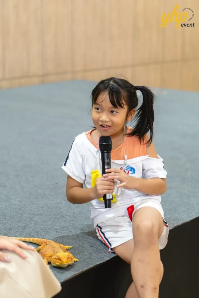 Super Kids Explorer: An Exciting Adventure at Bukit Bantayan 24 A young girl holds a microphone next to a bearded dragon on a stage during a pet show talent segment
