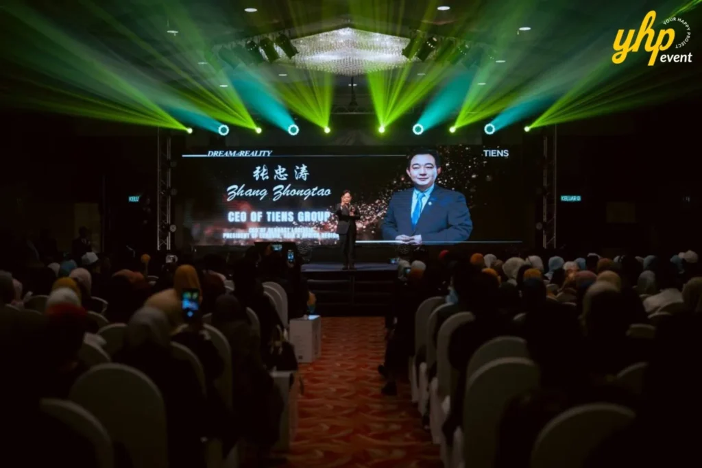 TIENS Sabah Convention l Borneo Royale Hotel Tawau 2 Presenter addresses a seated audience at TIENS conference while a large screen displays CEO Zhang Shongtao