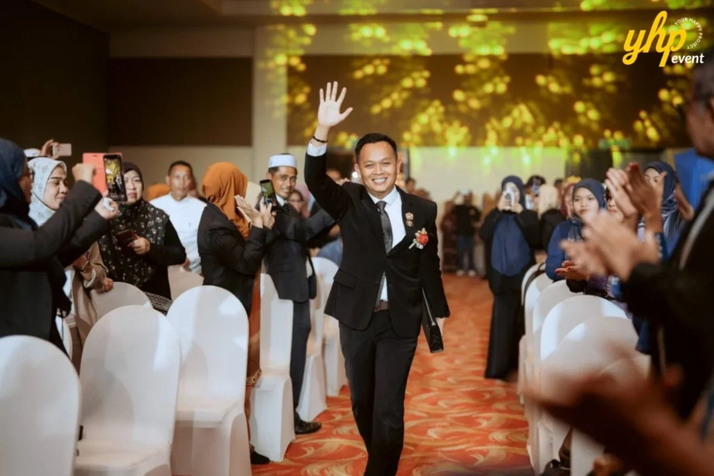 TIENS Sabah Convention l Borneo Royale Hotel Tawau 4 Smiling attendee walks down the aisle at TIENS event, waving to guests seated on both sides of the hall