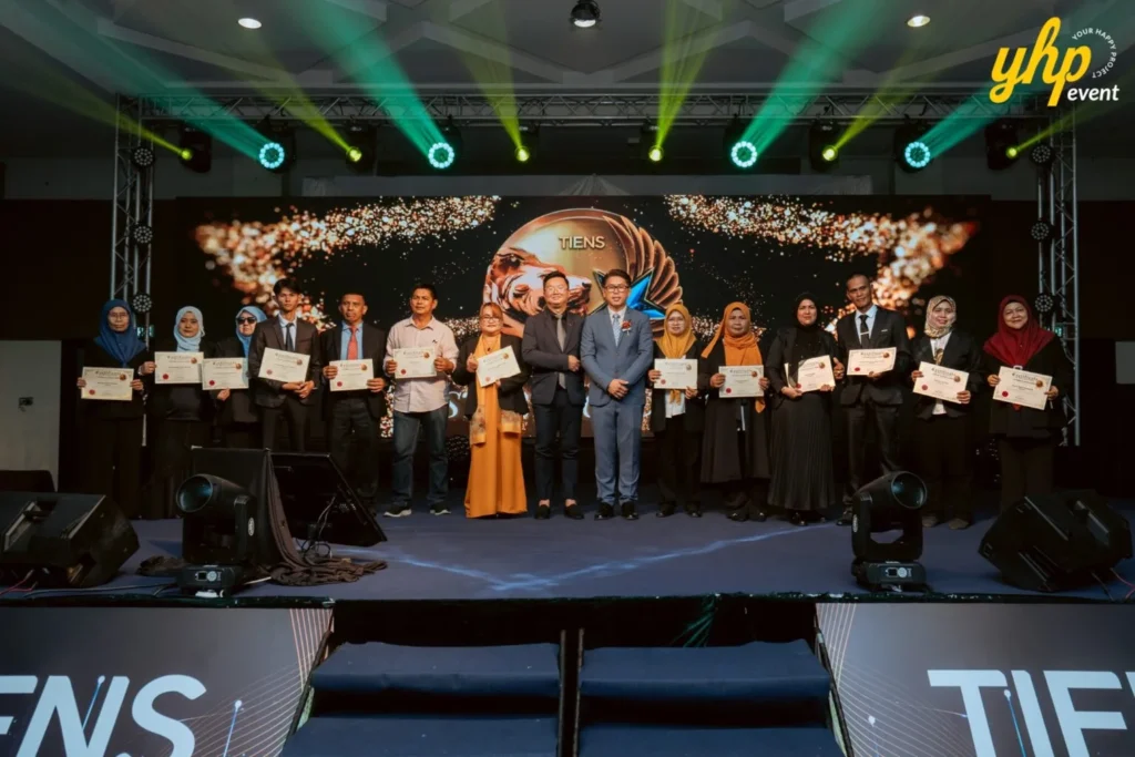 TIENS Sabah Convention l Borneo Royale Hotel Tawau 7 Certificate recipients line up on TIENS stage for a group photo with presenters under green event lights