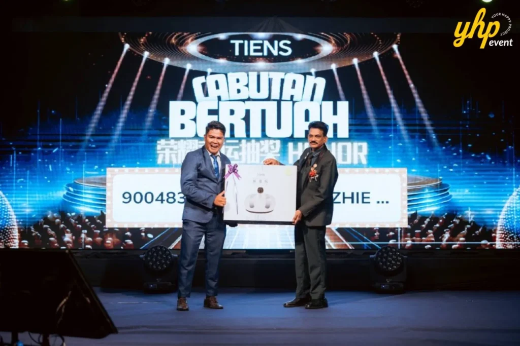 TIENS Sabah Convention l Borneo Royale Hotel Tawau 10 Award handover during TIENS lucky draw event as two suited men pose onstage before a large illuminated backdrop