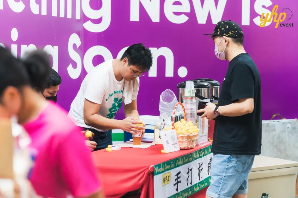#TooHuattoHandle Lunar New Year Celebration 13 Local Sabahan Vendor preparing drinks at a red-covered stall with beverage urn, basket display, and purple event backdrop