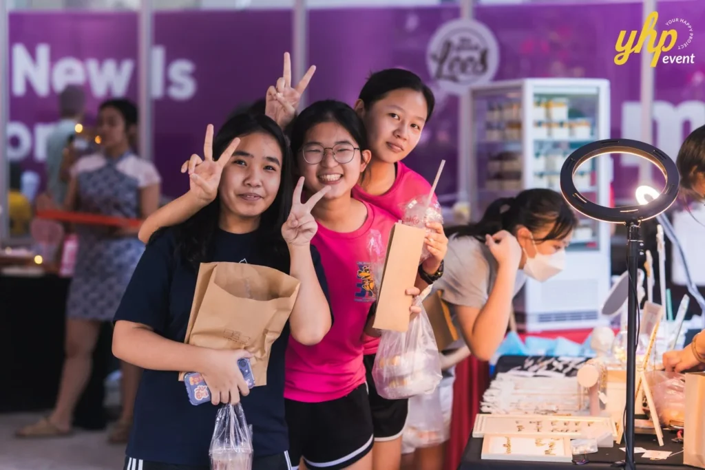 #TooHuattoHandle Lunar New Year Celebration 14 Three girls smiling and making peace signs while holding market purchases beside a jewelry and accessories stall