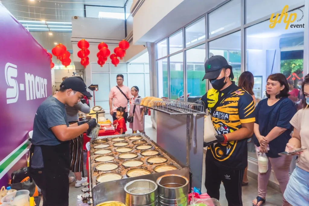 #TooHuattoHandle Lunar New Year Celebration 17 Street food vendors cooking mini pancakes at a busy indoor market stall under red lanterns and bright event lighting