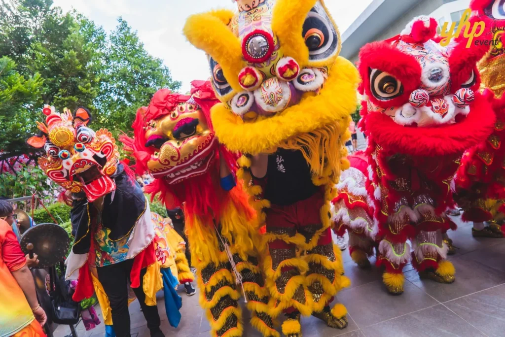 #TooHuattoHandle Lunar New Year Celebration 3 Colorful lion dance costumes leaning toward the camera during a Chinese cultural festival with musicians and spectators