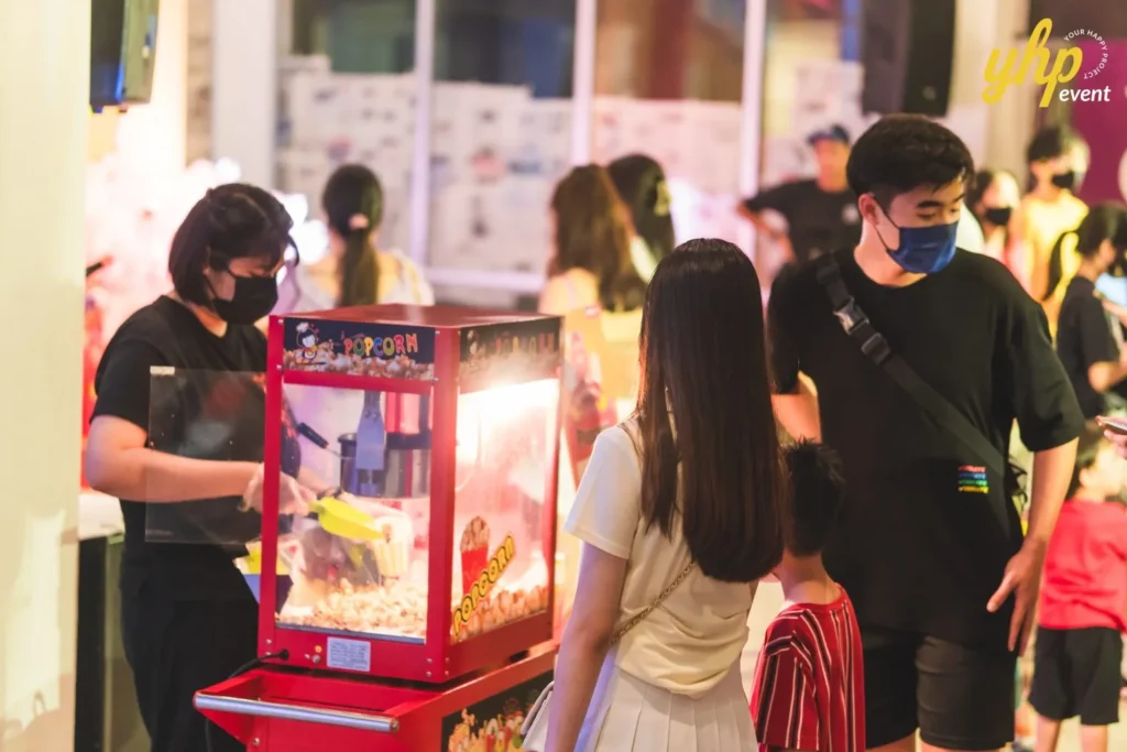#TooHuattoHandle Lunar New Year Celebration 21 Popcorn vendor serving snacks to parents and children at a warm-lit night market inside a busy community venue