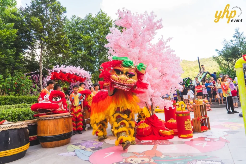 #TooHuattoHandle Lunar New Year Celebration 4 Red lion dance performer posing beside pink blossom decor and festival drums at a lively daytime community celebration