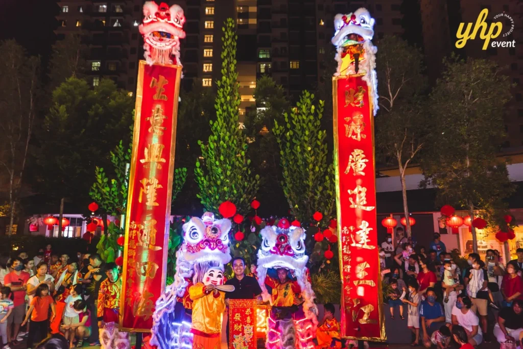 #TooHuattoHandle Lunar New Year Celebration 8 Crowd gathered for a nighttime lion dance ceremony with tall red banners, lanterns, and illuminated costumes