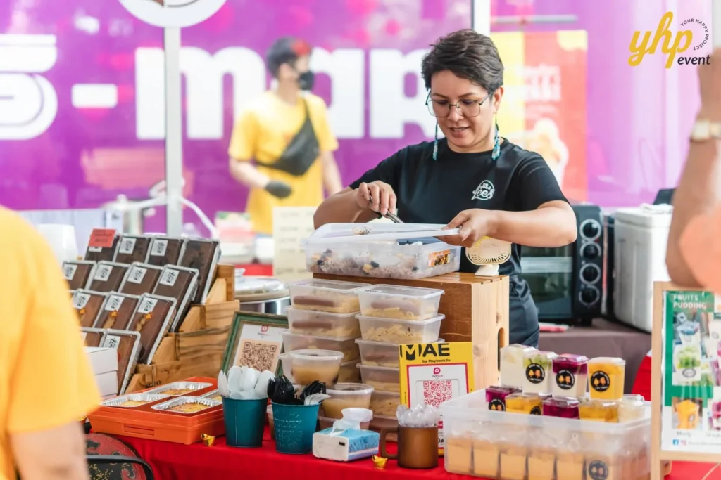 #TooHuattoHandle Lunar New Year Celebration 10 Local Sabahan Food vendor arranging prepared meals and desserts at a market stall with QR code signs and colorful background